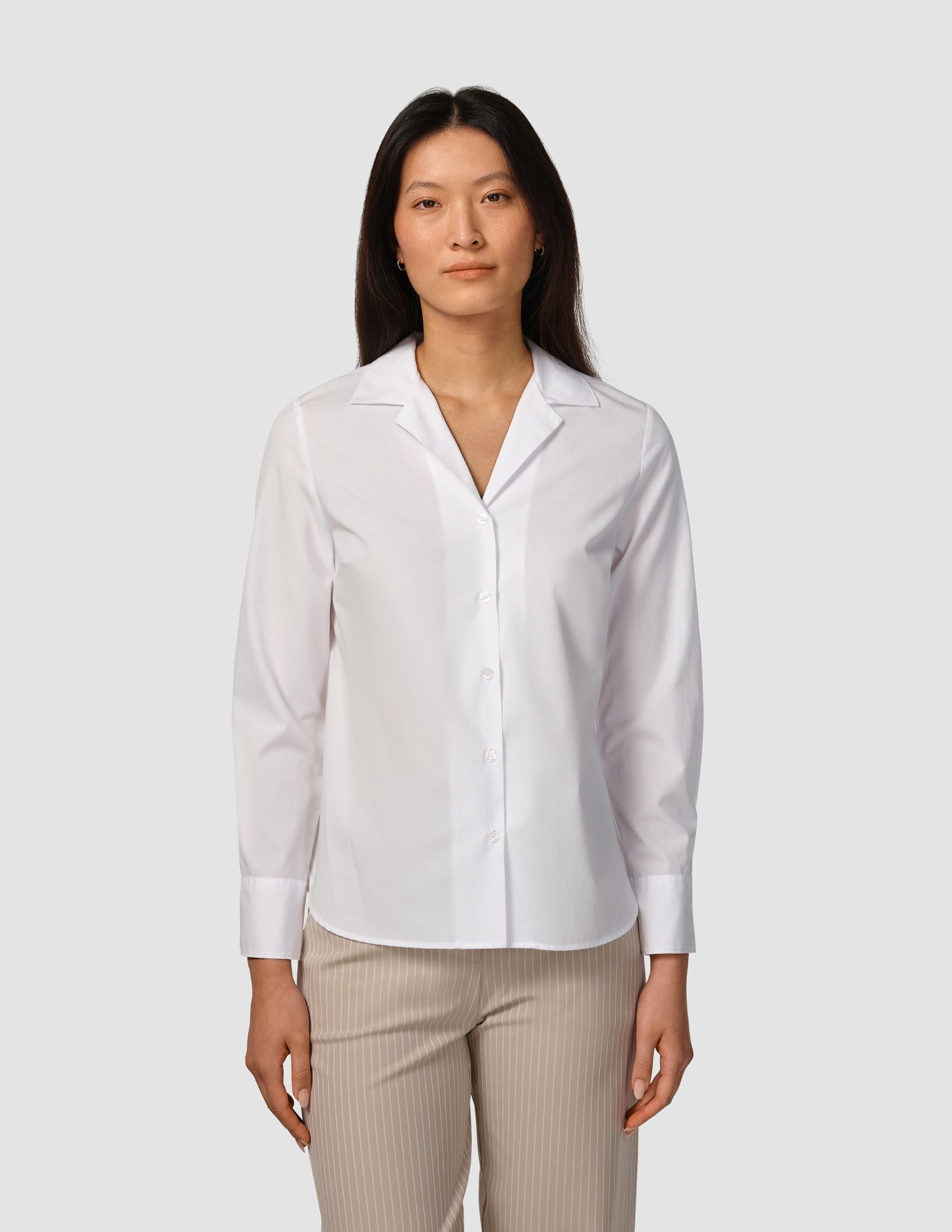 Eine Frau, die ein weißes „Madison Shirt White“ mit gekerbtem Kragen und eine beige Nadelstreifenhose trägt.